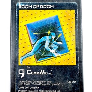 May include: A vintage black video game cartridge for the Atari system, labeled "ROOM OF DOOM." The label features a blue figure in a futuristic setting against a yellow background. Includes text: "By CommaVid Inc."