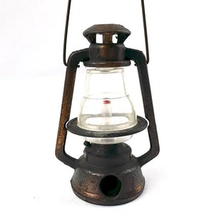 May include: A vintage metal pencil sharpener shaped like a lantern with a clear plastic glass and a red tip. The sharpener has a handle on top and a round hole on the bottom for sharpening pencils.