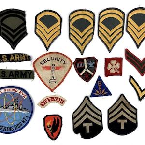 Könnte beinhalten: Eine Sammlung von Vintage-Militärabzeichen und -Insignien, darunter Winkel, Abzeichen und Einheitsabzeichen. Die Abzeichen weisen verschiedene Farben, Designs und Texte wie "U.S. ARMY", "SECURITY BOEING" und "USS HAWKINS DDR 873" auf.
