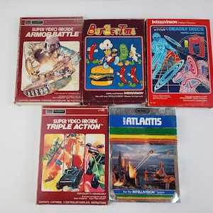 May include: Five vintage video game cartridges for the Intellivision console. The cartridges are in their original packaging and feature colorful artwork. The games include Armor Battle, Burger Time, Tron Deadly Discs, Triple Action, and New Atlantis.