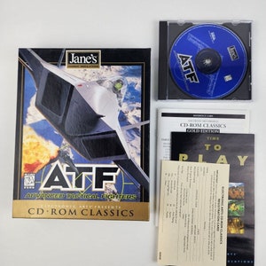 May include: A CD-ROM case for the computer game Jane's Advanced Tactical Fighters (ATF) Gold Edition. The case features a blue and white image of a fighter jet on the front. The game is a combat simulation game.