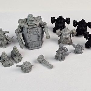 May include: A collection of miniature gray and black robot figures, including large, boxy robots and smaller, detailed models with various weapon attachments. The figures are arranged on a white surface.