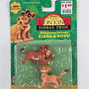 Puede incluir: Un juego de juguetes empaquetado con dos figuras de leones de El Rey León de Disney: El orgullo de Simba. El embalaje incluye el texto "Frollicking Friends Kiara & Kovu" y "New Characters!". Las figuras son de color marrón y beige.