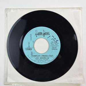 May include: A black vinyl record with a light blue label featuring the text "WAN SONG" and "TRAMPLED UNDER FOOT" by Led Zeppelin. The record is in a clear plastic sleeve.