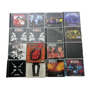 May include: A collection of Metallica CDs, featuring album art with various designs. The CDs showcase album titles like "Kill 'Em All", "Ride the Lightning", and "Load". The covers display a range of colors and graphics, including band logos and illustrations.