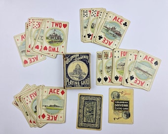 May include: A set of vintage Columbian Souvenir playing cards with a blue box featuring a building illustration. The cards display various architectural scenes within circular frames, red and black suit symbols, and the text Columbian Souvenir Playing Card Co.