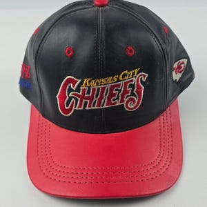 Könnte beinhalten: Eine schwarz-rote Kansas City Chiefs Baseballkappe. Die Kappe zeigt den Teamnamen in Rot und Weiß mit einem roten Schirm. Die Oberseite der Kappe ist schwarz mit roten Akzenten und das NFL-Logo an der Seite.