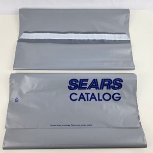 Peut inclure: Deux enveloppes d'expédition en plastique gris avec le texte "SEARS CATALOG" imprimé en bleu sur le devant. Les enveloppes ont un joint en ruban adhésif blanc et un symbole de recyclage.