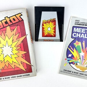 May include: Three vintage video game cartridges from Parker Brothers. The "Reactor" game box features a red and yellow explosion graphic. The "Meet the Challenge" box has a colorful starburst design. The game cartridges are for Atari & Sears video game systems.