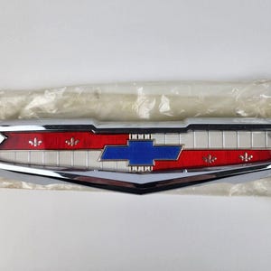 Puede incluir: Un emblema Chevrolet cromado con un diseño rojo, blanco y azul. El emblema presenta un logotipo de corbata de lazo estilizado y acentos de flor de lis.