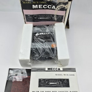 May include: A Mecca MCR-1400B in-dash car cassette player with AM/FM radio, packaged in a white and black box with styrofoam inserts. Includes an owner's manual and a small plastic bag containing a glass fuse, all featuring the Mecca brand name.