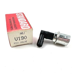 Op de afbeelding: Een PCV-klep met een zwarte rubberen elleboog en een zilveren metalen uiteinde. De klep staat naast een rode en beige doos met het "STANDARD"-logo en de tekst "U190 PCV VALVE".