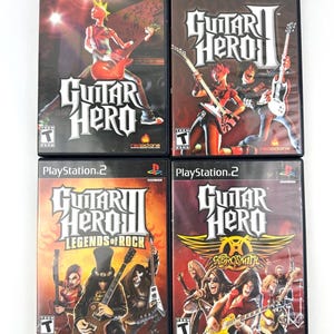 May include: Four PlayStation 2 video game cases. The games are Guitar Hero, Guitar Hero II, Guitar Hero III: Legends of Rock, and Guitar Hero: Aerosmith. Each case features colorful graphics of guitar players and the game title.