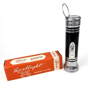 May include: A vintage black and chrome flashlight with a silver handle and a matching orange box. The box reads "Spotlight" and "Chrome Plated". The flashlight is a classic design, likely from the mid-20th century.