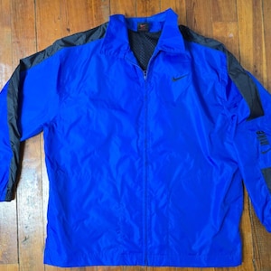May include: A blue and black windbreaker jacket with a zipper closure and a Nike logo on the front. The jacket has black accents on the sleeves and a mesh lining.