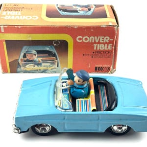 Pode incluir: Carro de brinquedo conversível azul vintage com uma figura de motorista. O carro tem pneus pretos e interior preto. A caixa diz "CONVERTIBLE FRICTION" e "FOR CHILDREN AGES 3+ UP MOVABLE HANDS".