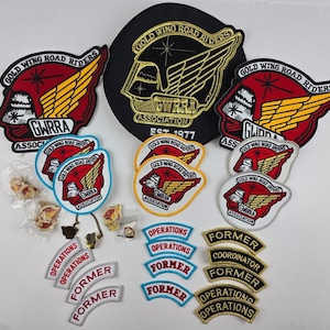 May include: A collection of Gold Wing Road Riders Association patches and pins. Includes large black and red embroidered patches, smaller circular patches with red, white, and yellow accents, and curved rocker patches with text like Operations and Former.