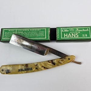 May include: A vintage straight razor with a green and white box. The razor has a yellow and brown marbled handle and a silver blade. The box says "Otto Deutsch Hans 5/8" and "Made in Solingen, Germany".