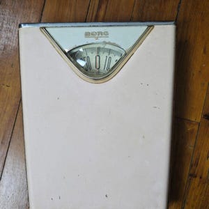 Puede incluir: Una báscula de baño vintage blanca y plateada con un dial redondo que dice "BORG".