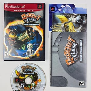 May include: A PlayStation 2 video game set featuring "Ratchet & Clank: Going Commando." The set includes the game case, disc, and manual. The case is black with the game title and characters. The disc has the game title and PlayStation 2 logo.