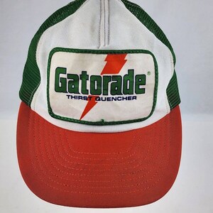 May include: A white, green, and red mesh trucker hat with a vintage Gatorade logo patch. The patch features a lightning bolt and the text "Gatorade" and "Thirst Quencher".