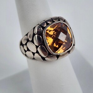 May include: A silver ring with a large, faceted, orange gemstone set in a textured, pebble-like band.