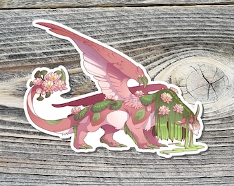 May include: A sticker featuring a pink and green mythical creature with large wings, horns, and a long tail. The creature is adorned with lotus flowers and green foliage. The background is a wooden surface.