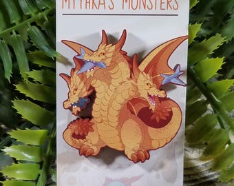 May include: A three-headed dragon with orange scales and red wings. The dragon is eating a blue fish. The image is on a white card with the text "Mythka's Monsters" and "Etsy.com/shop/mythka".