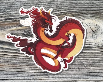 May include: A red and yellow dragon with black accents, curled up in a circle. The dragon has a long, flowing mane and tail. The dragon is on a wooden background.