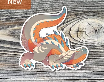 May include: A sticker featuring a cartoon monster with orange, gray, and blue accents. The monster has a long tail and spiky back. The word "New" is in a brown rectangle in the upper left corner.