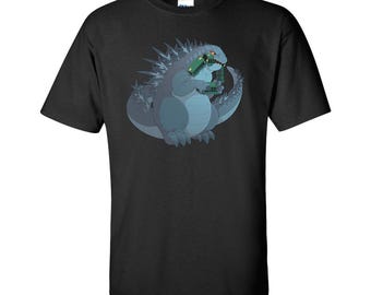 May include: Black t-shirt with a cartoon illustration of a gray Godzilla-like monster eating a stack of green books.