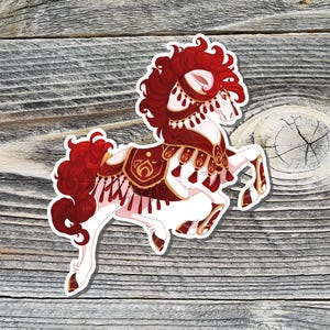 May include: A sticker featuring a white horse with red and maroon accents. The horse has a flowing red mane and tail, and is adorned with decorative maroon and gold tack. The sticker is on a wooden background.