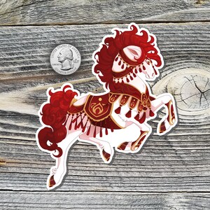 May include: A sticker featuring a white horse with red and gold decorative elements. The horse has a flowing red mane and tail, and is adorned with tassels and ornate designs. A U.S. quarter is next to the sticker for size reference.