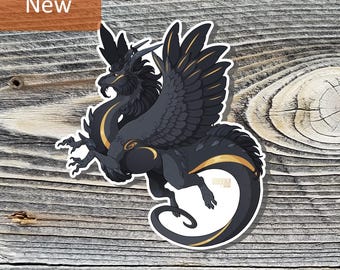 May include: A die-cut sticker featuring a dark charcoal gray dragon with large feathered wings, golden yellow accents along the chest, tail, and wing feathers, and a small horn on its head. The word New is printed in white on an orange rectangle.