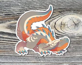 May include: A colorful sticker featuring a stylized illustration of a fantasy creature. The creature has a long tail, orange and blue accents, and a detailed design. The sticker is on a wooden surface.