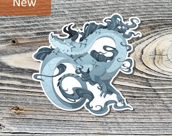 May include: A die-cut sticker featuring a stylized, serpentine dragon in shades of light and dark blue. The dragon has a long, winding body, sharp claws, and flowing, cloud-like appendages, all outlined in white against a wood grain background.