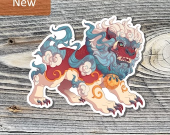 May include: A die-cut sticker featuring a stylized guardian lion creature with a red body, cream-colored legs, and a flowing blue mane. The creature has sharp teeth, dark claws, and a round orange ornament around its neck with swirling cloud patterns.