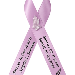 May include: A lavender awareness ribbon featuring a small, light-colored praying hands emblem at the center. The left side reads "Forever In Our Hearts Angela L. Sheldon" and the right side reads "Sunrise 08/11/2000 Sunset 10/02/2025" with a small black wing icon.