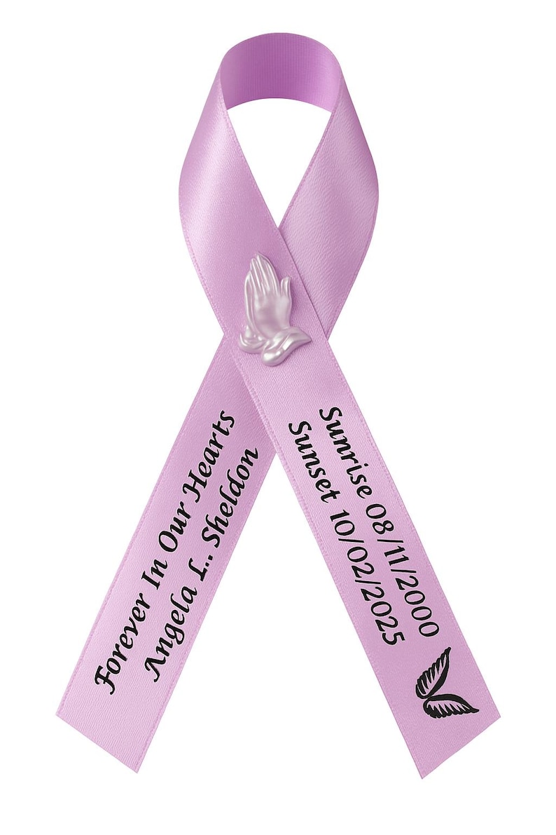 May include: A lavender awareness ribbon featuring a small, light-colored praying hands emblem at the center. The left side reads "Forever In Our Hearts Angela L. Sheldon" and the right side reads "Sunrise 08/11/2000 Sunset 10/02/2025" with a small black wing icon.
