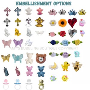 May include: A collection of small decorative embellishments featuring crosses, angels, crowns, flowers, hearts, butterflies, teddy bears, baby bottles, pacifiers, moons, ducks, and bees in various colors and finishes with the text EMBELLISHMENT OPTIONS.