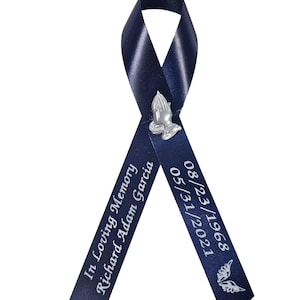 May include: A navy blue satin ribbon folded into a loop, featuring a silver-toned praying hands charm at the center. The left tail is printed with "In Loving Memory Richard Adam Garcia" and the right tail with "08/23/1968 05/31/2021" and a dove.