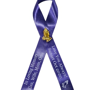 May include: A purple awareness ribbon featuring a gold-toned praying hands pin at the center. The left tail is printed with "In Loving Memory Elsa, Wife, Mom, Oma" and the right tail features "Love You Always! Sunset Oct 2020" with a small icon.