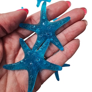 May include: A collection of five blue glass starfish, with a textured surface, are held in a hand.