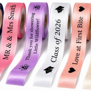 May include: Six spools of satin ribbon in navy blue, pink, lavender, white, peach, and cream. Each ribbon features black printed text and icons, including phrases like Summit Senior, MR & Mrs Smith, Thank you for showering Little Wildflower!, Class of 2026, Love at First Bite, and Congratulations! Jason & Jennifer.