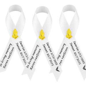 May include: Three white satin ribbons arranged in a loop, each featuring a gold-toned praying hands emblem. The text reads: In loving memory, Karen vanItten, Sunrise 2/23/1955, Sunset 10/7/2025. A small black butterfly graphic is printed at the bottom.