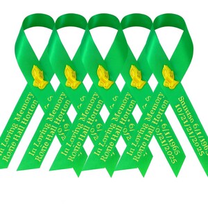 May include: Five bright green satin ribbons arranged in a row, each featuring a gold-colored praying hands emblem. The ribbons are printed with the text In Loving Memory, Rome Hall Horton, and the dates 6/1/1965 and 10/21/2025 in gold lettering.
