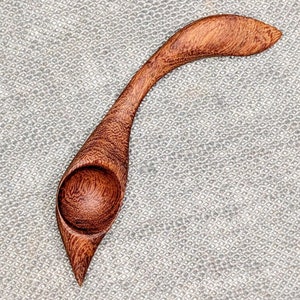 Könnte beinhalten: Ein Holzlöffel mit einem einzigartigen gebogenen Griff und einer abgerundeten Schüssel. Der Löffel ist aus dunkelbraunem Holz gefertigt und hat eine natürliche Oberfläche.