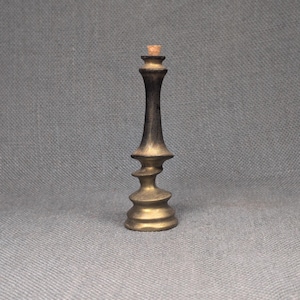 Puede incluir: Un tapón de botella decorativo con diseño de rey de ajedrez. El tapón es de latón y tiene un acabado bronce oscuro con una parte superior de corcho. El diseño presenta un cuerpo en espiral y una parte superior en forma de corona.