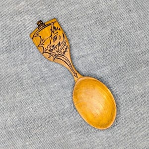 May include: A wooden spoon with a dragon design carved into the handle. The spoon is made of light brown wood and has a rounded bowl.