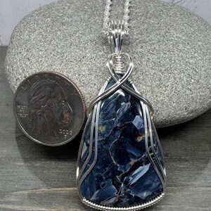 May include: A silver wire wrapped pendant featuring a blue and grey tiger's eye gemstone. The pendant is hanging from a silver chain.